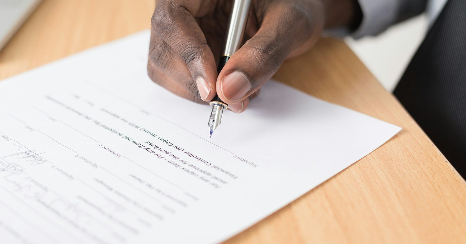 Mão assinando um documento sobre uma mesa de madeira