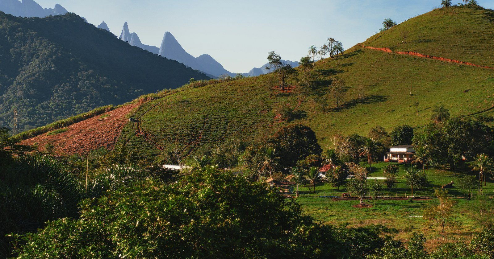 Casas espalhadas em um morro verde, com montanhas ao fundo