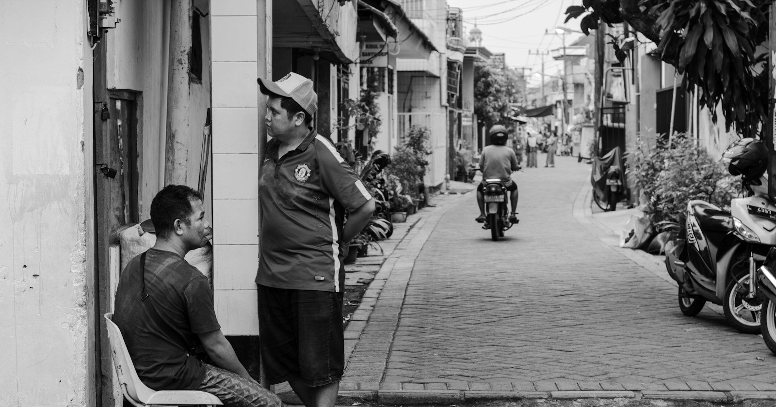 Foto em preto e branco de moradores conversando na porta de casa em uma rua estreita
