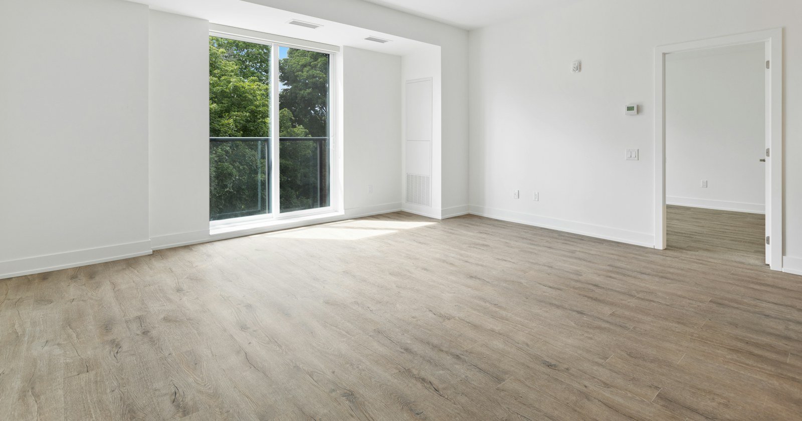 Apartamento novo e vazio, com piso claro e porta de vidro para a sacada